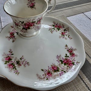 May include: A white porcelain teacup and saucer set with a floral pattern. The cup has a scalloped rim and a handle. The saucer has a scalloped edge and a floral design around the rim.