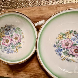 May include: A set of two vintage teacups with a green and white floral design. The cups have a gold rim and a delicate floral pattern.