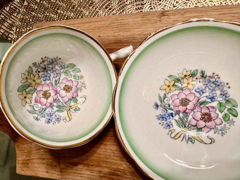 May include: A set of two vintage teacups with a green and white floral design. The cups have a gold rim and a delicate floral pattern.