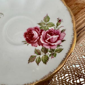 Pu&ograve; includere: Un piattino in porcellana bianca con un bordo dorato e un motivo floreale con rose rosa e rosse. Il piattino &egrave; decorato con foglie verdi e un bordo dorato.