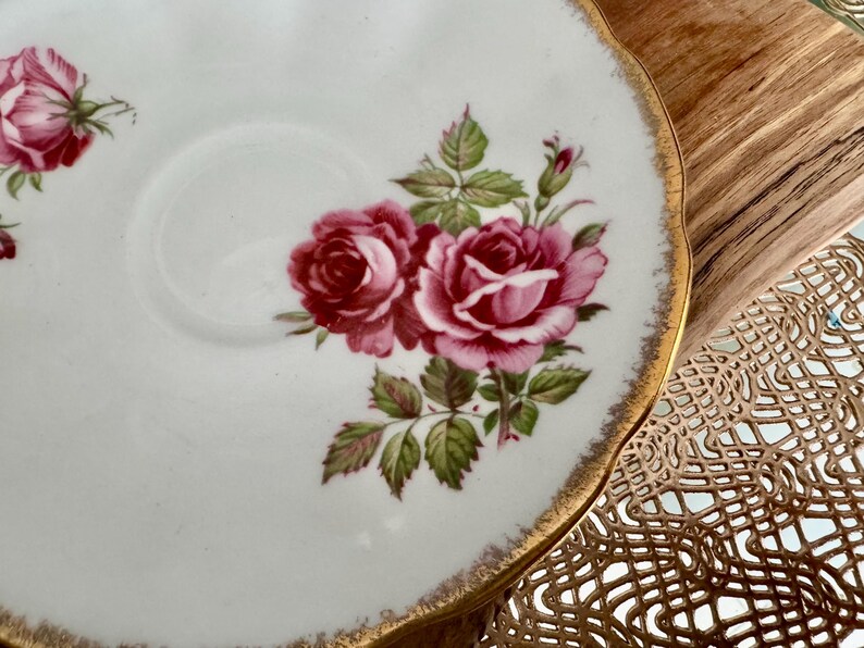 Pu&ograve; includere: Un piattino in porcellana bianca con un bordo dorato e un motivo floreale con rose rosa e rosse. Il piattino &egrave; decorato con foglie verdi e un bordo dorato.