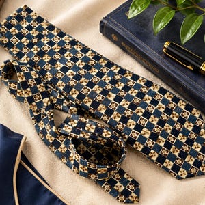 May include: A necktie featuring a repeating geometric checkerboard pattern in shades of navy blue, cream, and brown. The design consists of alternating solid navy squares and cream squares containing a small brown floral-like motif.