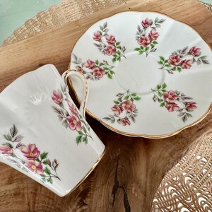 May include: A white teacup and saucer with a floral pattern. The cup and saucer have a gold trim around the edges. The flowers are pink and green.