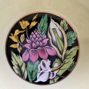 May include: A black and white floral design with pink, yellow, and green accents. The design is on a white background with a gold rim.