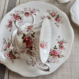 May include: A white teacup and saucer set with a floral pattern. The saucer has a scalloped edge and a gold trim. The teacup has a floral pattern and a handle.