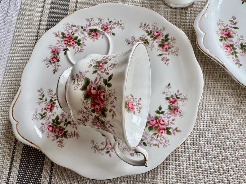 May include: A white teacup and saucer set with a floral pattern. The saucer has a scalloped edge and a gold trim. The teacup has a floral pattern and a handle.