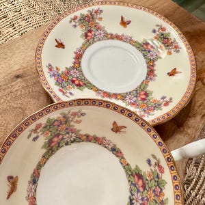 May include: Two vintage teacups with floral and butterfly designs. The cups are white with gold trim and feature a delicate floral pattern with colorful butterflies.