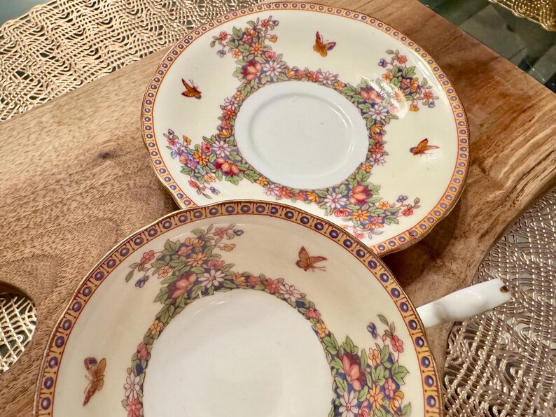 May include: Two vintage teacups with floral and butterfly designs. The cups are white with gold trim and feature a delicate floral pattern with colorful butterflies.