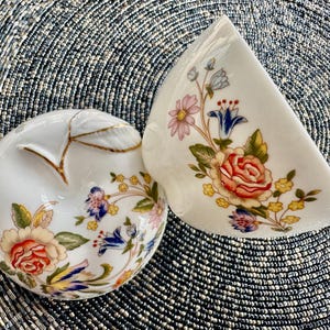 K&ouml;nnte beinhalten: Zwei wei&szlig;e Porzellanschalen mit Blumendesigns. Die Schalen haben einen goldenen Rand und zeigen eine Vielzahl von Blumen in den Farben Rosa, Blau, Gelb und Rot.