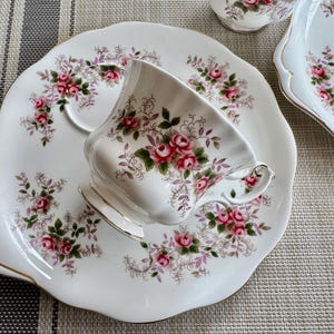 May include: A white teacup and saucer set with a floral pattern. The cup has a delicate floral design with pink roses and green leaves. The saucer has a scalloped edge and a matching floral pattern.