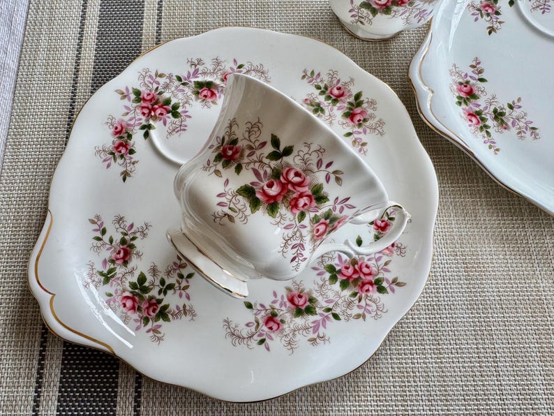 May include: A white teacup and saucer set with a floral pattern. The cup has a delicate floral design with pink roses and green leaves. The saucer has a scalloped edge and a matching floral pattern.