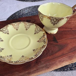 May include: A yellow teacup and saucer set with gold trim and a delicate floral pattern. The teacup has a handle and the saucer is round.