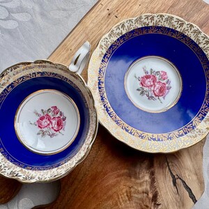 May include: A vintage teacup and saucer set with a cobalt blue background and gold trim. The set features a floral design with pink roses.