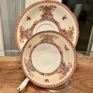 May include: A vintage teacup and saucer set with a floral pattern. The cup and saucer are white with a gold trim and feature a delicate floral design with butterflies. The saucer has a scalloped edge.
