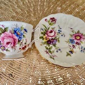 May include: A white teacup and saucer set with a floral pattern. The cup and saucer are decorated with pink, blue, and yellow flowers on a white background.