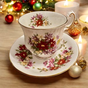 May include: A white teacup and saucer with a floral pattern featuring red, pink, and yellow flowers. The cup and saucer have a gold trim.
