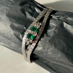 May include: A silver chain bracelet with a cluster of emerald green and clear stones.