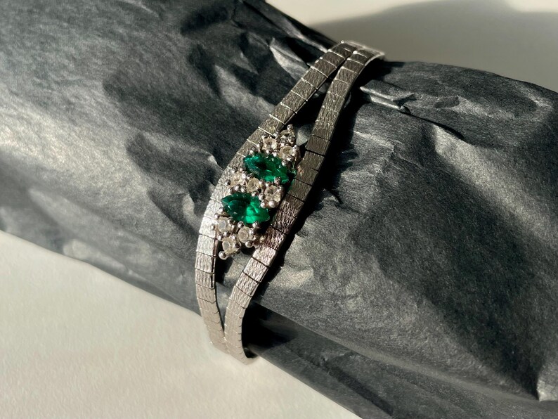 May include: A silver chain bracelet with a cluster of emerald green and clear stones.