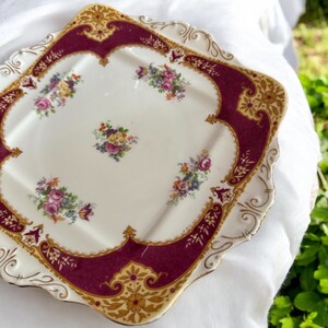 May include: A square, white ceramic serving plate with a burgundy and gold border. The plate has a scalloped edge and is decorated with floral designs.