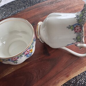 Pu&ograve; includere: Un set di zuccheriera e lattiera in porcellana bianca con un motivo floreale in tonalit&agrave; rosa, blu e giallo. Il set ha un bordo dorato.