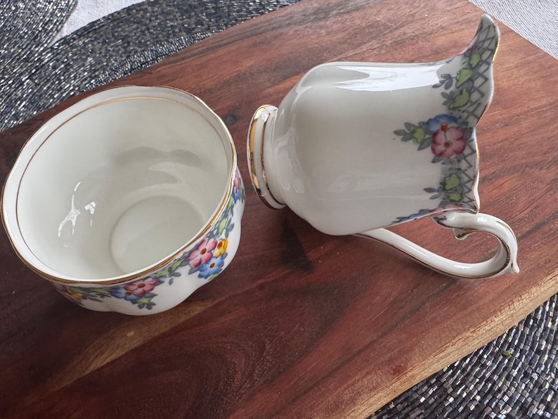 Pu&ograve; includere: Un set di zuccheriera e lattiera in porcellana bianca con un motivo floreale in tonalit&agrave; rosa, blu e giallo. Il set ha un bordo dorato.