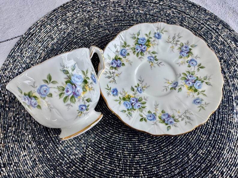 Pu&ograve; includere: Una tazza da t&egrave; e un piattino bianchi con un motivo floreale blu e bianco. La tazza e il piattino hanno un bordo dorato.