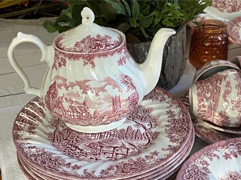 Pu&ograve; includere: Un servizio da t&egrave; bianco e bordeaux con teiera, piatti e tazze da t&egrave;. Il set presenta un design paesaggistico dettagliato. La teiera &egrave; sopra una pila di piatti. Le tazze da t&egrave; sono su piattini. Il set &egrave; in ceramica.
