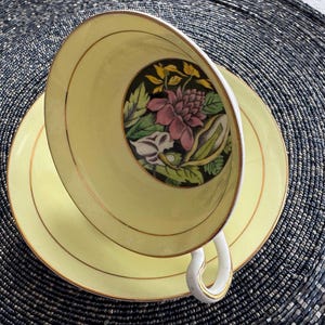 May include: A yellow teacup and saucer with a floral design. The cup and saucer have a gold trim.