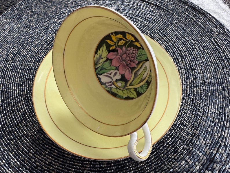 May include: A yellow teacup and saucer with a floral design. The cup and saucer have a gold trim.