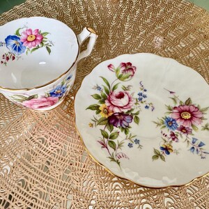 May include: A white teacup and saucer with a floral pattern. The cup has a gold rim and a handle. The saucer has a scalloped edge.