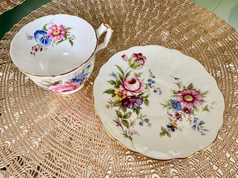 May include: A white teacup and saucer with a floral pattern. The cup has a gold rim and a handle. The saucer has a scalloped edge.