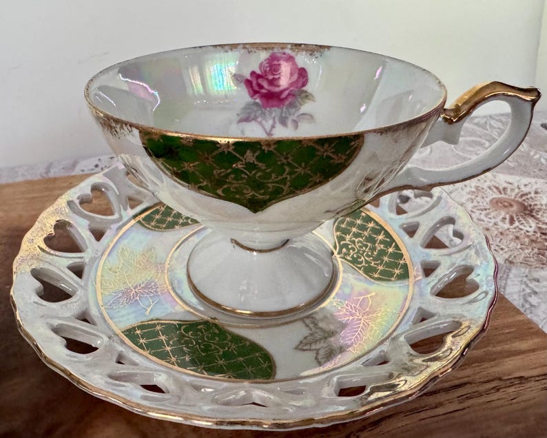 Puede incluir: Un juego de taza y platillo de t&eacute; vintage. La taza blanca presenta un dise&ntilde;o de rosa rosa y ribetes dorados. El platillo tiene un borde en forma de coraz&oacute;n y detalles en verde y dorado. El juego est&aacute; dise&ntilde;ado para tomar el t&eacute; y ocasiones especiales.
