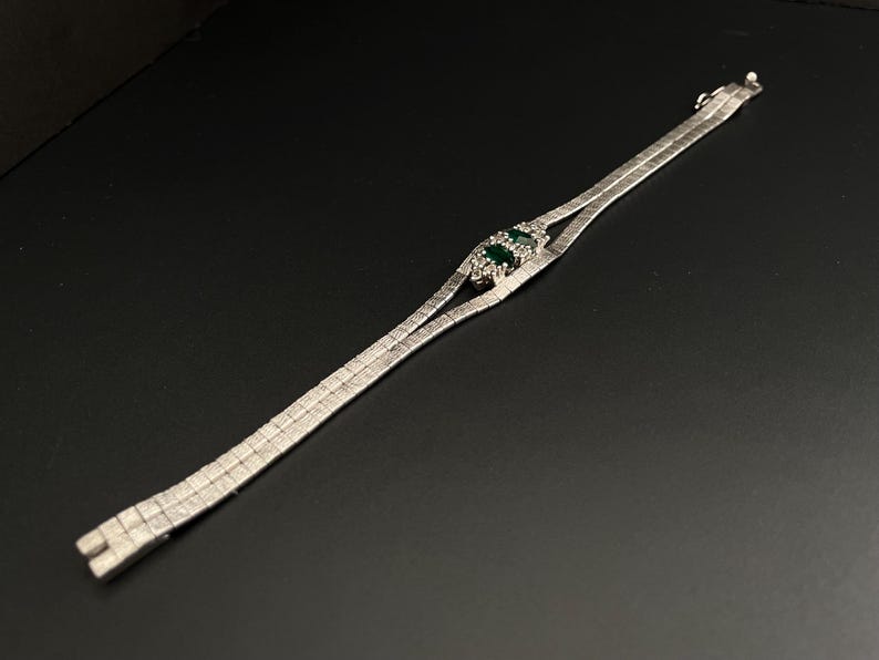 May include: A silver chain bracelet with a green stone set in a silver frame.