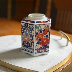 Peut inclure: Un pot d&eacute;coratif en c&eacute;ramique de forme carr&eacute;e avec un motif floral. Le pot pr&eacute;sente des couleurs rouge, bleu et blanc. Le pot est pos&eacute; sur un plateau en marbre blanc avec une bordure dor&eacute;e.