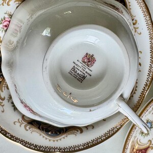 May include: A close-up of a white teacup and saucer set with gold trim and floral accents. The teacup is upside down, revealing the Paragon England mark. The set has a vintage aesthetic.
