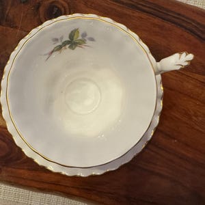 Puede incluir: Una taza de t&eacute; y un platillo blancos con un borde dorado y un dise&ntilde;o floral. La taza de t&eacute; tiene un asa delicada y un borde festoneado.