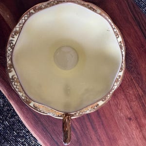 May include: A yellow teacup with a gold rim and floral design. The cup has a scalloped edge and a small handle.