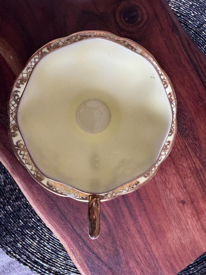 May include: A yellow teacup with a gold rim and floral design. The cup has a scalloped edge and a small handle.