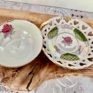 Puede incluir: Juego de porcelana de dos piezas con un cuenco y un plato con motivo de rosa. El cuenco es blanco con borde dorado y una rosa roja. El plato tiene borde en forma de coraz&oacute;n, detalles verdes y un dise&ntilde;o central de rosa. Sobre una superficie de madera.