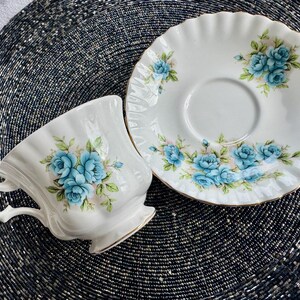 May include: A white teacup and saucer set with a blue floral pattern. The teacup has a scalloped rim and a delicate handle. The saucer has a scalloped edge and a floral design around the rim.