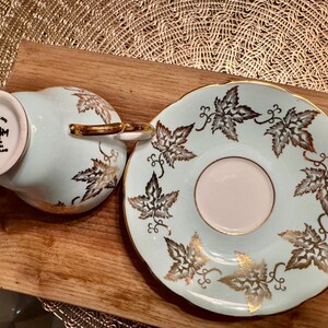 May include: A light blue teacup and saucer set with a gold leaf design. The teacup has a white underside with the text "Sutherland Made China Made in England 3181".