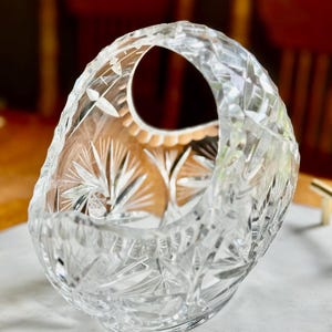 May include: A clear, cut-glass basket with a handle. The basket features intricate starburst and geometric patterns. The handle has a large opening. The basket is likely used for decorative purposes or to hold small items.