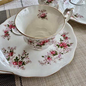 May include: A white teacup and saucer set with a floral pattern. The teacup has a gold rim and the saucer has a scalloped edge.
