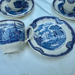 Puede incluir: Juego de t&eacute; vintage de cer&aacute;mica azul y blanca. La taza presenta un paisaje con una iglesia, mientras que el platillo muestra un castillo. El conjunto est&aacute; sobre un mantel blanco, mostrando el dise&ntilde;o cl&aacute;sico.