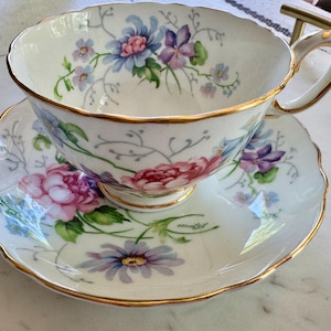 Pu&ograve; includere: Servizio da t&egrave; bianco con decorazioni floreali. La tazza e il piattino presentano fiori rosa, viola e blu e foglie verdi. I bordi sono rifiniti in oro. Ideale per t&egrave; o caff&egrave;.