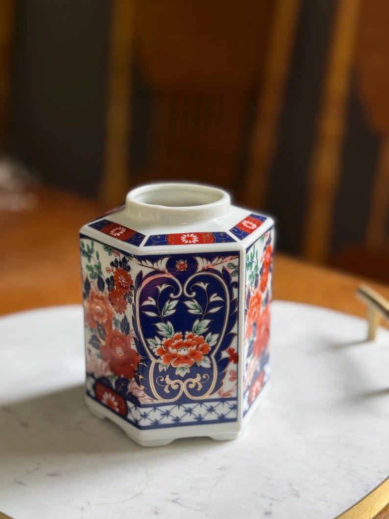 Peut inclure: Un vase hexagonal en c&eacute;ramique avec une base blanche, orn&eacute; d'un motif floral vibrant en rouge, bleu et vert. Le vase pr&eacute;sente un design d&eacute;taill&eacute; avec un fond bleu et des accents floraux rouges, mettant en valeur une esth&eacute;tique classique.