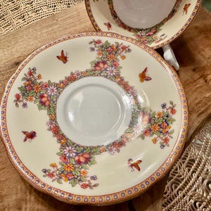 May include: A white porcelain saucer with a floral pattern in shades of red, yellow, and green. The saucer has a gold rim and a delicate butterfly design.