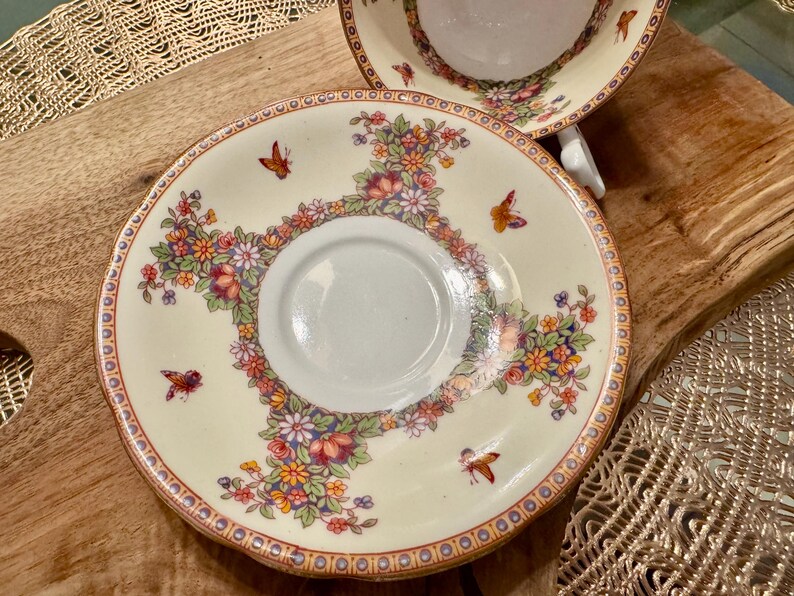 May include: A white porcelain saucer with a floral pattern in shades of red, yellow, and green. The saucer has a gold rim and a delicate butterfly design.