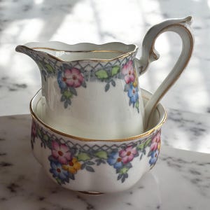 Pu&ograve; includere: Un set di brocca per la panna e zuccheriera in porcellana bianca con un motivo floreale in tonalit&agrave; di rosa, blu, giallo e verde. Il set ha un bordo dorato.