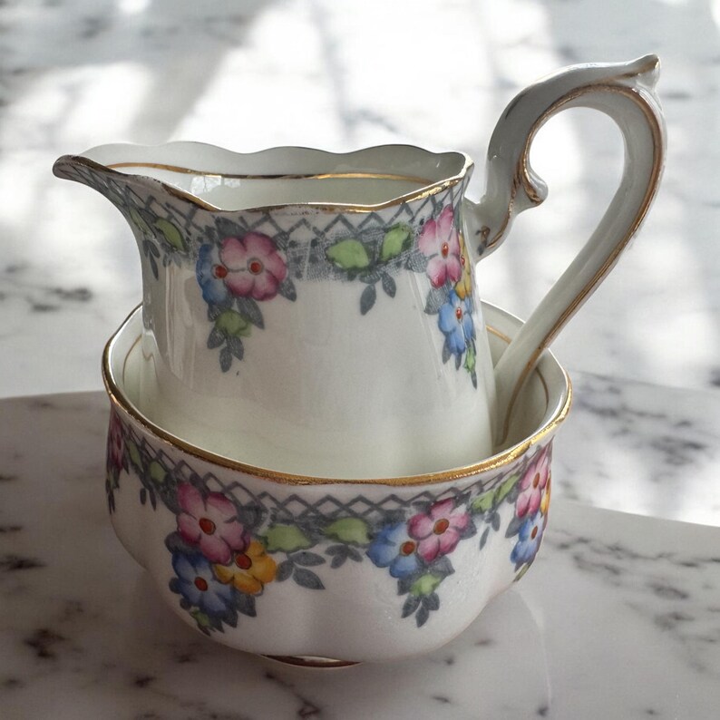 Pu&ograve; includere: Un set di brocca per la panna e zuccheriera in porcellana bianca con un motivo floreale in tonalit&agrave; di rosa, blu, giallo e verde. Il set ha un bordo dorato.